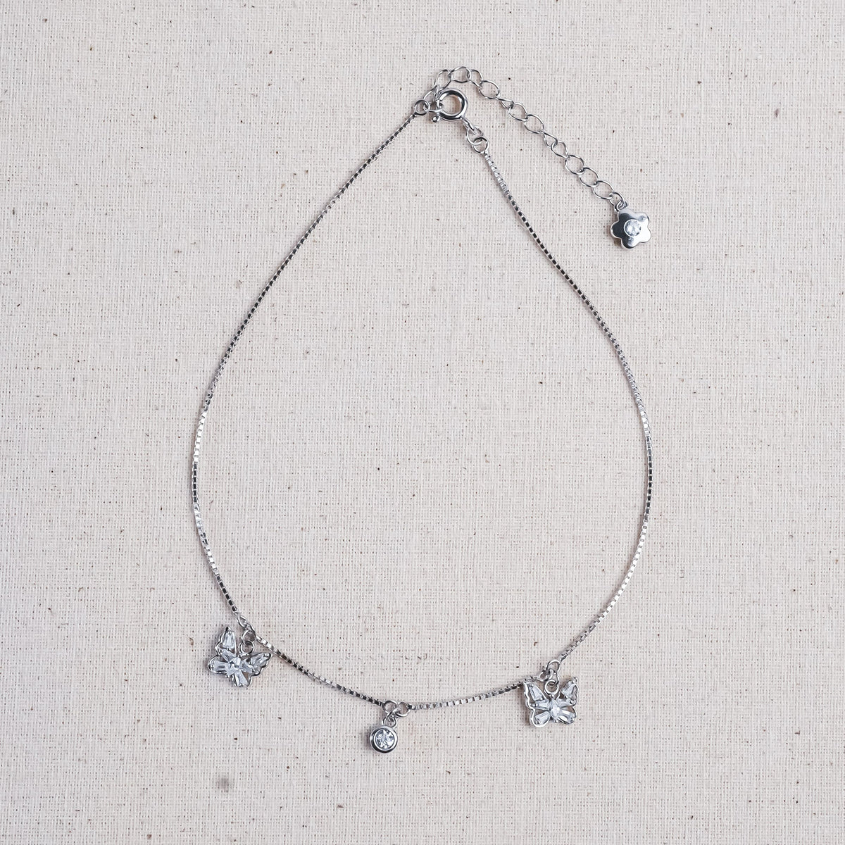 A delicate silver chain anklet featuring three butterfly charms and a small central round charm.