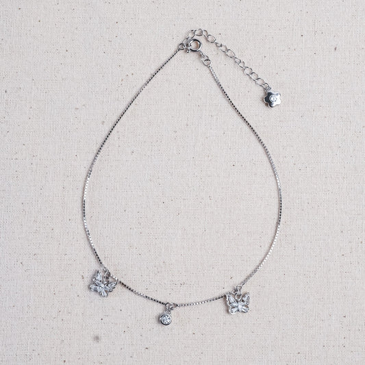 A delicate silver chain anklet featuring three butterfly charms and a small central round charm.